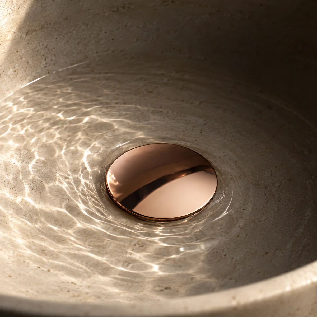 Bonde de Lavabo Clic-Clac en or rose brossé, installée au fond d’une vasque en pierre